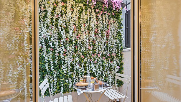 En matplats med ett bord dukat för två personer, omgivet av vita stolar, med en vägg prydd med ett blommönster som bakgrund.