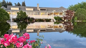Une grande maison avec un bassin aux eaux calmes, entourée de verdure et de fleurs roses.