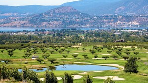 Un parcours de golf avec des bunkers de sable, un étang et une vue sur une ville et des montagnes au loin.