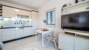Una cocina moderna con armarios blancos, una mesa de comedor con sillas y un televisor de pantalla plana grande montado en la pared.