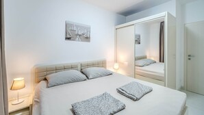 Una cama bien tendida con cabecera, lámpara de noche, manta doblada, una obra de arte en la pared y un espejo que refleja parte de la habitación.
