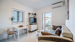 Una sala de estar moderna con un sofá, una mesa de comedor con sillas, un televisor y un balcón con vistas.