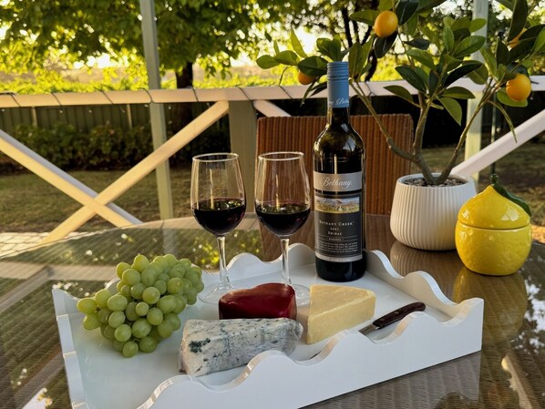 A table with a bottle of wine, two glasses, a bunch of grapes, a piece of cheese, and a knife.