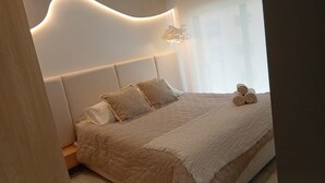 Un dormitorio con cama, almohadas, una colcha y toallas enrolladas.