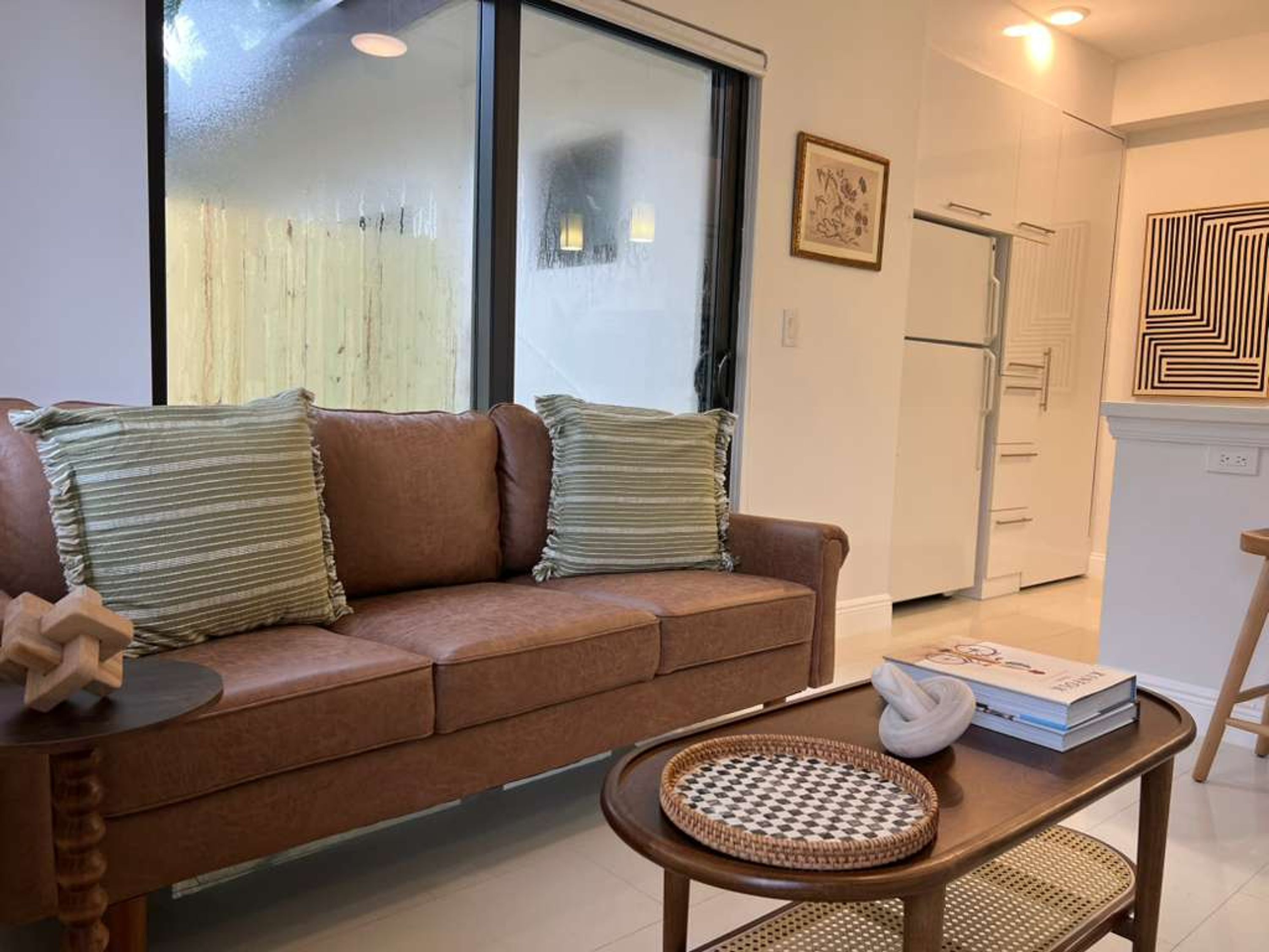 A living room with a brown sofa, two pillows, a woven tray, and a book on a wooden table.