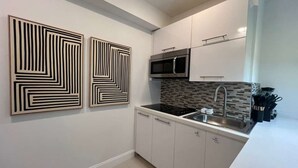 Una cucina moderna con mobili bianchi, un piano di lavoro nero, un lavello in acciaio inossidabile e due opere d'arte astratte appese alle pareti.