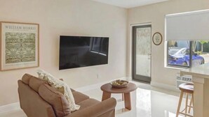 Un soggiorno moderno con una TV a schermo piatto, un divano marrone, un tavolino rotondo e una grande finestra con vista su un'auto blu.