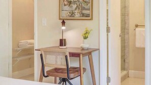 A bathroom with a shower, a towel rack, a framed floral painting, a small table with a lamp, and a chair. - Open-concept Urban Stay (Fort Lauderdale)