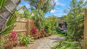 Un giardino con vialetto sterrato, recinzione in legno e diverse piante.