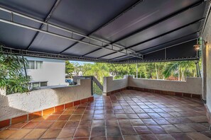 A covered outdoor area with tiled flooring, a metal roof, and a view of greenery and buildings in the background. - Victoria Park Oasis Walk to las Olas Beach (Fort Lauderdale)