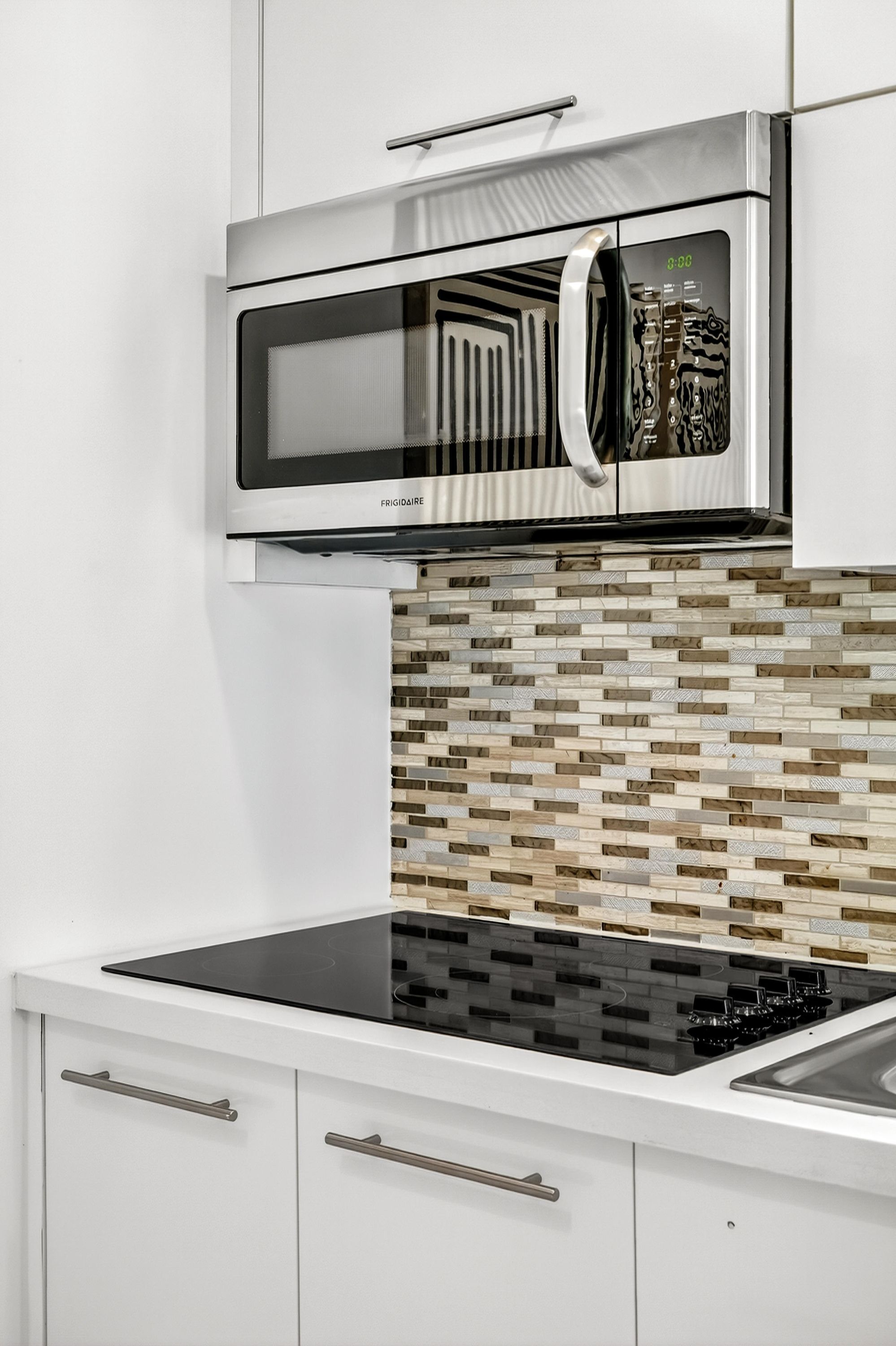 A kitchen with a stainless steel microwave, a black induction cooktop, and a tiled backsplash.