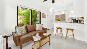 A modern living room with a brown leather sofa, a wooden coffee table, and a large window with a view of greenery. - Chic Modern Studio With Queen Bed (Fort Lauderdale)