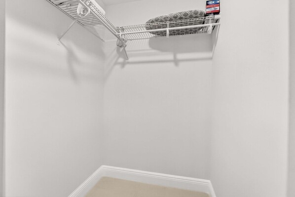 A corner of a room with a white wall, a white baseboard, and a metal shelf unit with a patterned pillow and a box on it. - Chic Modern Studio With Queen Bed (Fort Lauderdale)