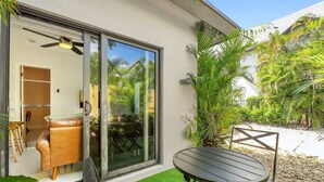 A modern outdoor patio with a glass door leading to a room, a round table, and chairs. - Chic Modern Studio With Queen Bed (Fort Lauderdale)