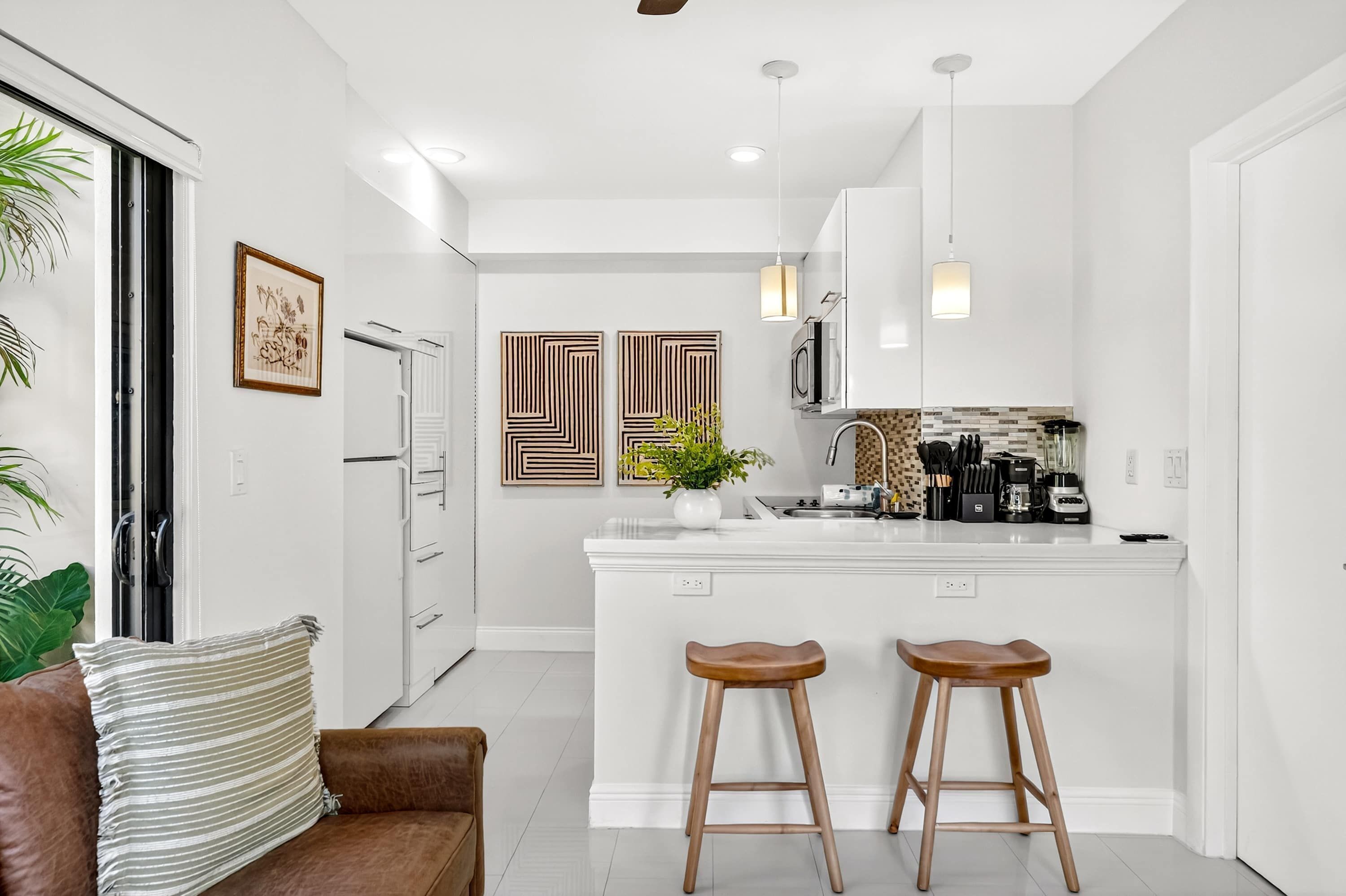 A modern kitchen with white cabinetry, a central island with stools, pendant lighting, and a large window.