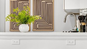 A kitchen with two wooden stools, a white countertop, a vase with green plants, and two wall-mounted light fixtures. - Chic Modern Studio With Queen Bed (Fort Lauderdale)