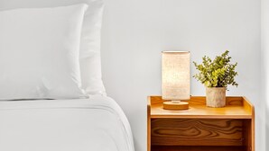 A neatly made bed with white bedding, a bedside table with a lamp and a potted plant, and a framed botanical artwork on the wall. - Chic Modern Studio With Queen Bed (Fort Lauderdale)