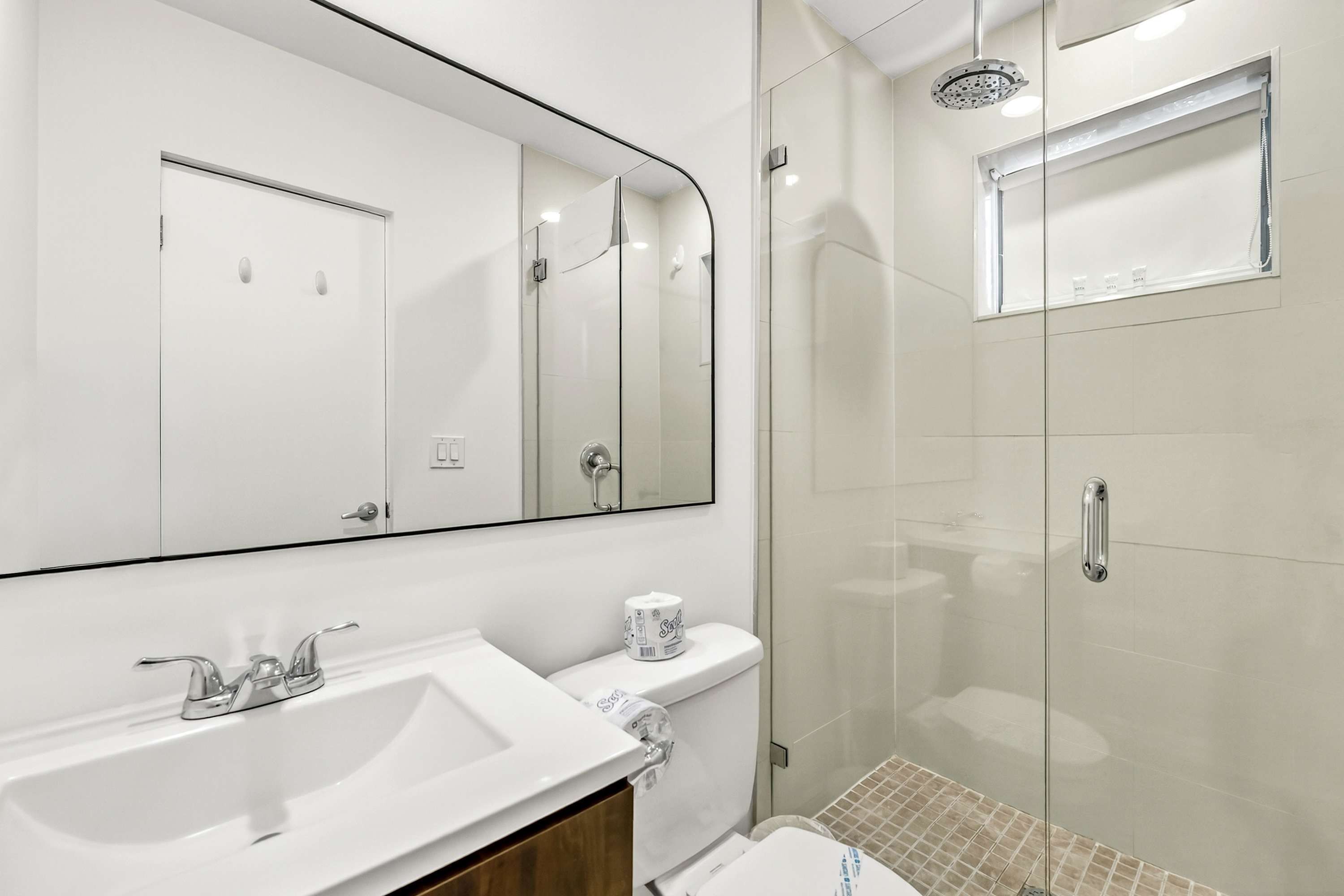 Un baño moderno con un espejo grande, un lavabo, un inodoro y una zona de ducha.