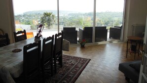 Zona pranzo con tavolo, sedie, un lampadario e vista panoramica attraverso ampie porte in vetro.