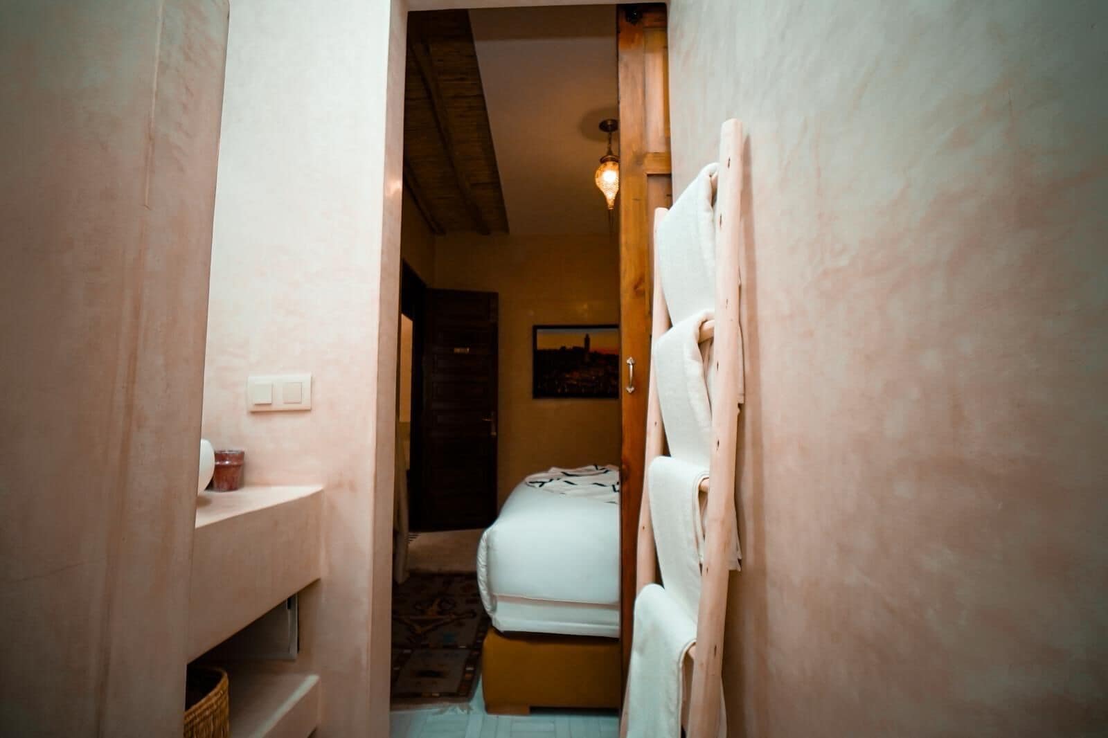 Un pasillo estrecho que conduce a un dormitorio con cama, cabecera de madera y lámpara colgante.