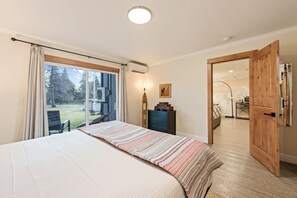 Ein Schlafzimmer mit einem großen Bett, einer Holztür und Gartenblick durch eine Schiebetür.