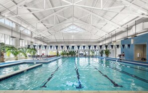 Una piscina interior con carriles delimitados, un techo alto con diseño geométrico y plantas en macetas alrededor del borde.