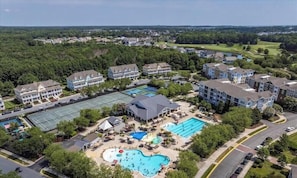 A residential area with multiple two-story houses, a swimming pool, tennis courts, and a golf course in the background.