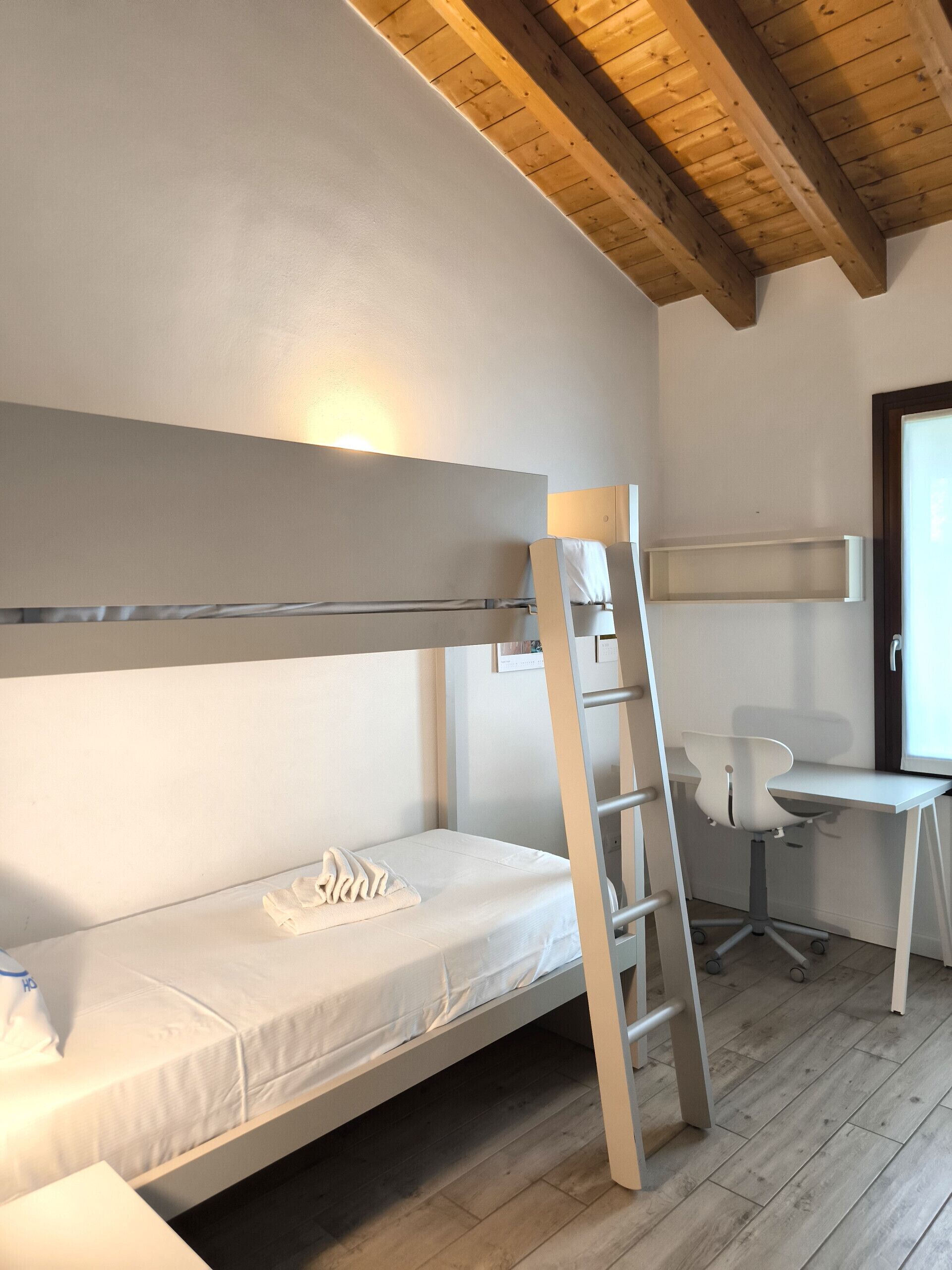 A bunk bed with a ladder, a desk with a chair, and a window.