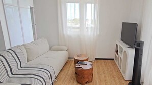 Ein modernes Wohnzimmer mit einer Couch, einem Couchtisch, einem Fernseher und einem Fenster mit durchsichtigen Vorhängen.
