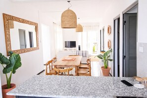 Eine moderne Küche mit Granit-Arbeitsplatte, einem Holzespeisetisch und Stühlen. Links befindet sich ein großer Spiegel, eine Hängeleuchte und ein Blumentopf.