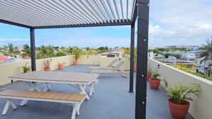 Eine Dachterrasse mit Tischen und Stühlen, Kübelpflanzen und Blick auf die Stadt.