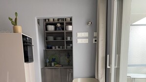 Une salle à manger avec une table recouverte d’une nappe bleue, des assiettes blanches et un pichet noir. Une chaise blanche et une petite plante en pot sont posées sur la table.