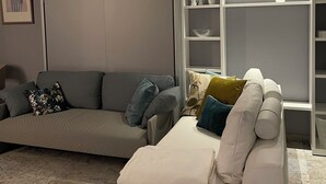 Un salon avec un canapé gris, un fauteuil blanc et une étagère blanche agrémentée d’objets décoratifs.