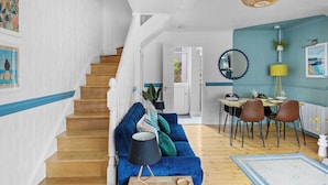 Una sala de estar moderna con un sofá azul, una escalera de madera, un comedor con sillas y una lámpara en el techo.