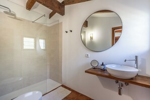 A bathroom with a glass-enclosed shower, a white toilet, a wooden vanity with a sink, and a round mirror. - Cal Roma, quiet villa with swimming pool and mountain views (IB)