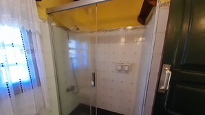 En dusch med glasväggar, ett handhållet duschmunstycke, en handdukshängare och en svart badmatta.