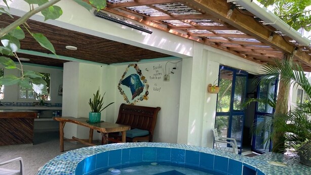 A swimming pool with mosaic tiles, a wooden pergola, a dining area with a table and chairs, and a wall with a decorative bird and text. - Private cabin with Jacuzzi, just one minute from the beach. (Bolívar)