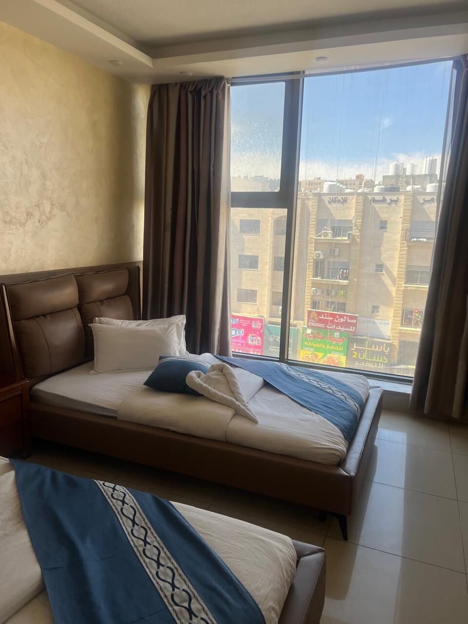 Une chambre d’hôtel avec un grand lit, un lit plus petit, une fenêtre avec des rideaux et une vue sur les bâtiments environnants.