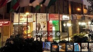 A modern building with vertical blue LED lights, flags, and a storefront with various signs. - almansi Hotels (Amman)