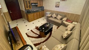 A modern living room with a sofa, a coffee table, and a kitchen area with cabinets and a microwave. - almansi Hotels (Amman)