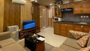A living room with a television, sofa, coffee table, and kitchen area with wooden cabinets and a tiled backsplash. - almansi Hotels (Amman)