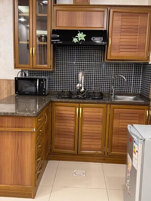 A kitchen with wooden cabinets, a microwave, a stove, and a sink. - almansi Hotels (Amman)