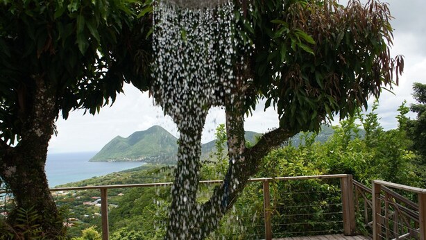 Una terraza de madera con vista a un paisaje costero, que incluye una montaña y una masa de agua.