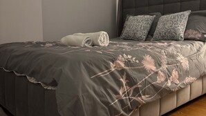 Un dormitorio con una cama grande, un cabecero, una ventana con cortinas, un cuadro enmarcado en la pared y suelo de madera.