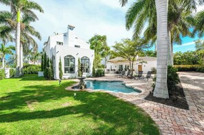 A white building with a swimming pool, surrounded by palm trees and a brick patio. - Beautiful Historic Ringling house! (Sarasota)