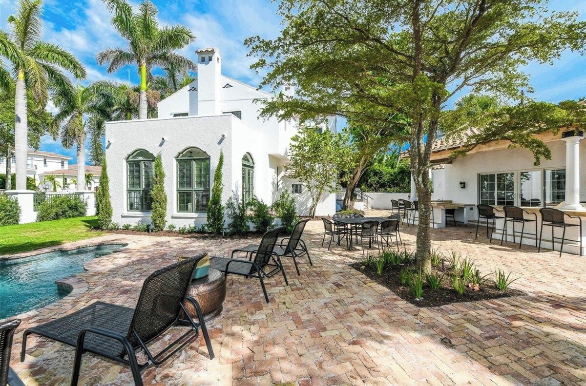 A white building with a pool, outdoor seating, and palm trees.