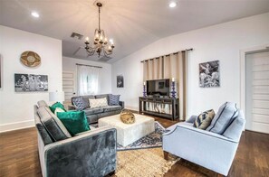 Ein Wohnzimmer mit einer Sofagarnitur, einem Couchtisch, einer TV-Konsole und Kunstwerken an den Wänden.