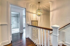 A hallway with a wooden staircase, white railings, and a chandelier. - Beautiful Historic Ringling house! (Sarasota)