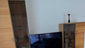 A living room with a TV, wooden cabinets, and a glass-top table. - Vacation apartment at the Diemelsee in Heringhausen (Diemelsee)