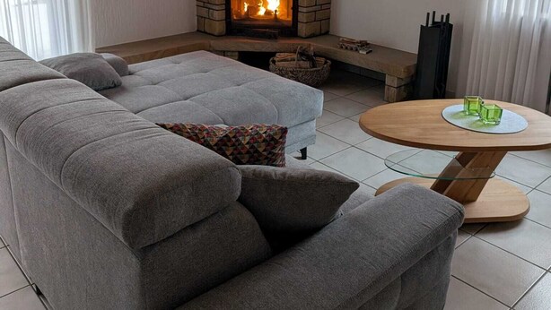 A modern living room with a stone fireplace, grey sectional sofa, and a round wooden coffee table. - Vacation apartment at the Diemelsee in Heringhausen (Diemelsee)